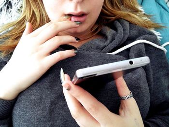 Midsection of woman with finger in mouth using phone