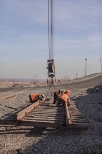 Workers adjusting chains on tracks against sky