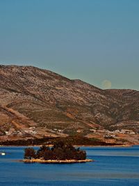 Scenic view of lake by mountain against clear blue sky