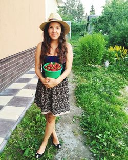 Portrait of young woman holding strawberries in container while standing in yard