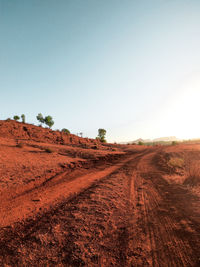 Dirt road amidst field against clear sky