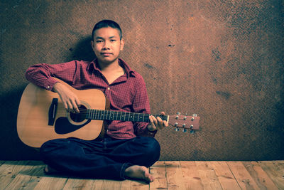 Full length of boy playing guitar against wall