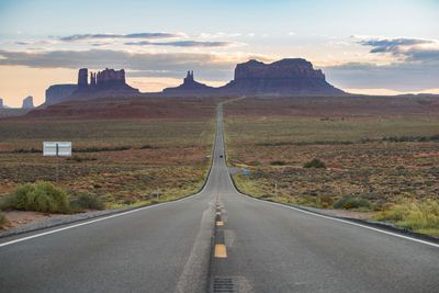 Empty road leading towards mountains against sky