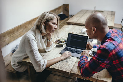 Multi-ethnic couple discussing while using laptop at table in coffee shop