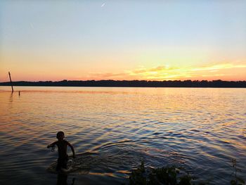 Boy standing in sea during sunset