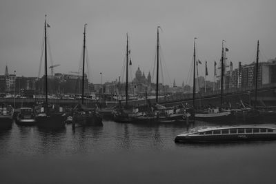 Boats moored at harbor against sky in city