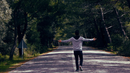 Rear view of young man with arms outstretched standing on road in forest