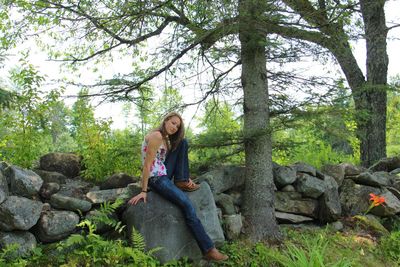 Smiling young woman standing on rock against trees