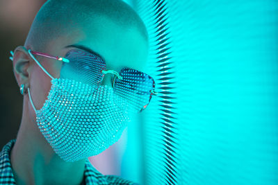 Portrait of young woman with shaved head wearing mask standing against abstract backgrounds