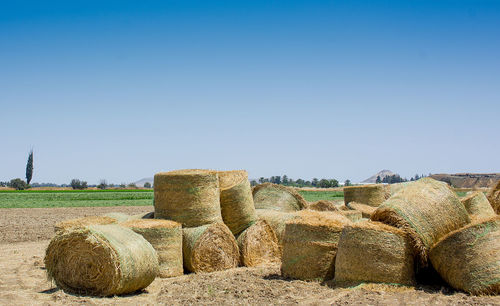Hay bales on field against clear blue sky