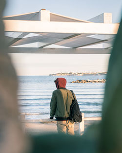 Rear view of man sitting on bridge over sea