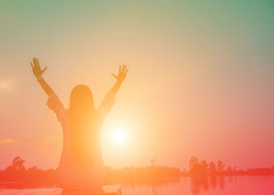 Silhouette woman with arms raised standing against sky during sunset