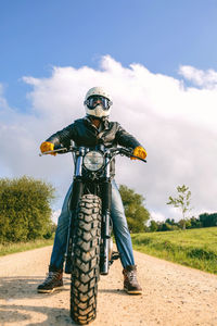 Man riding motorcycle on road by field against sky