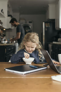 Girl having breakfast at table with father and sister in kitchen at home