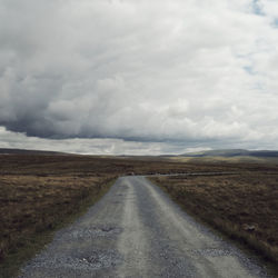 Road amidst landscape against moody sky