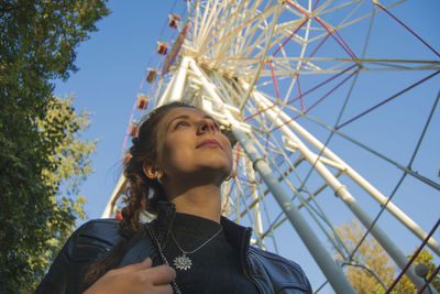 Low angle view of young woman against ferris wheel and sky