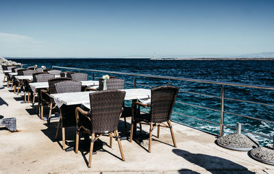 Chairs and table by sea against clear blue sky