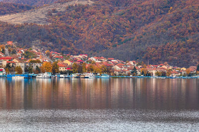 Scenic view of lake by trees and houses against mountain during autumn