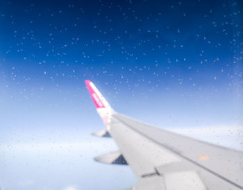 Aircraft wing seen through glass window against blue sky
