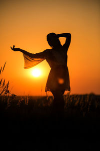 Silhouette woman standing on field against orange sky