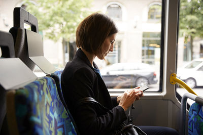 Side view of businesswoman using smart phone while sitting in bus
