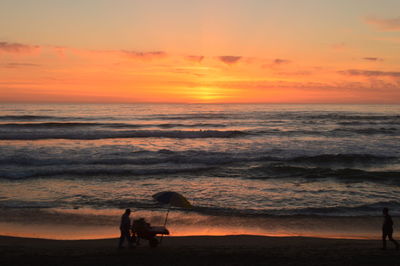 Silhouette people on beach against sky during sunset