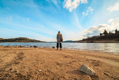 Rear view of woman standing on shore at beach against sky