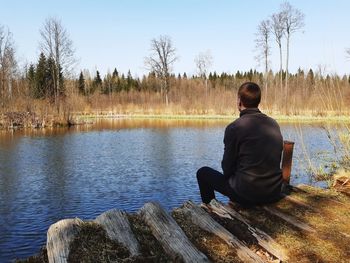 Rear view of man sitting by lake against sky