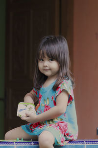 Portrait of cute girl sitting against wall