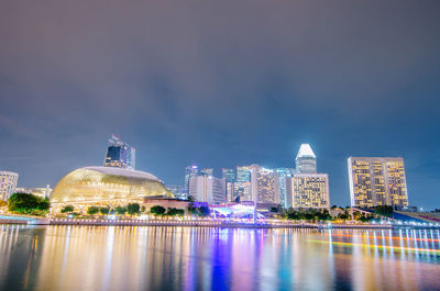 Illuminated buildings by river against sky in city at night