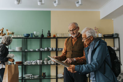 Male owner showing picture frame to senior customer in antique shop