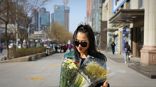Young woman wearing sunglasses and holding bouquet standing on street in city
