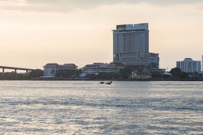 Sea by buildings against sky during sunset in city