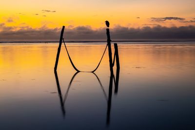 Silhouette man standing by lake against sky during sunset