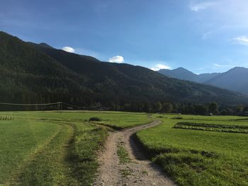 Pathway amidst grassy landscape leading towards mountains