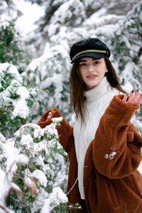 Portrait of young woman standing against flowers