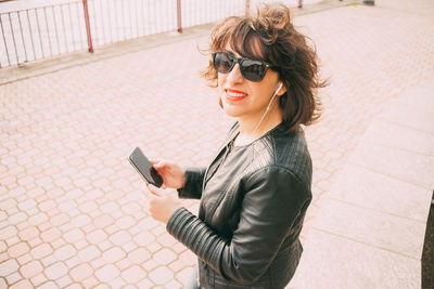 Portrait of smiling mid adult woman using mobile phone on footpath