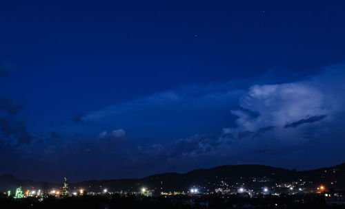 Illuminated cityscape against blue sky at night