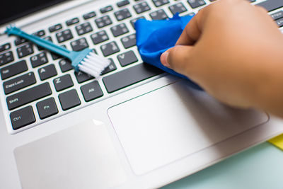 Cropped hand cleaning laptop with duster at table