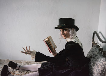 Young woman reading book against wall