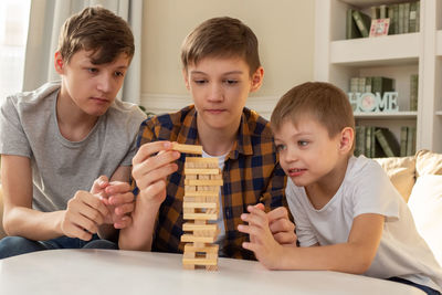 Three teen boy are playing a board game made of wooden rectangular blocks