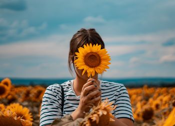 Portrait of man holding sunflower against bright sun