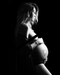 Side view of sensuous pregnant woman standing against black background