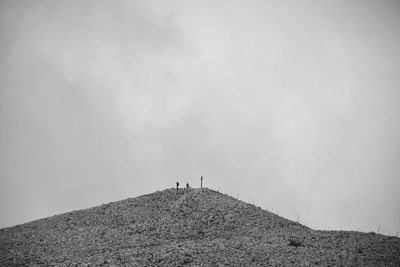 Low angle view of men standing on hill against sky