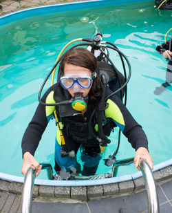 Portrait of woman with aqualung climbing ladder in swimming pool