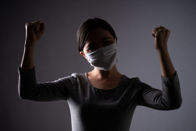 Portrait of young woman standing against gray background