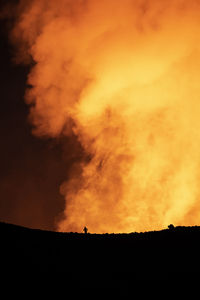 Silhouette of anonymous traveler standing against orange fume of active volcano in iceland