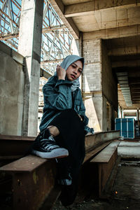 Full length portrait of muslim girl sitting against brick wall