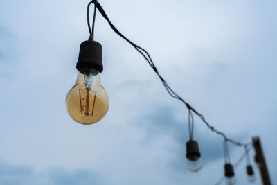 Low angle view of light bulb hanging against sky