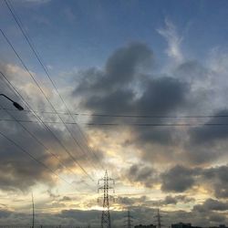 Low angle view of electricity pylon against cloudy sky